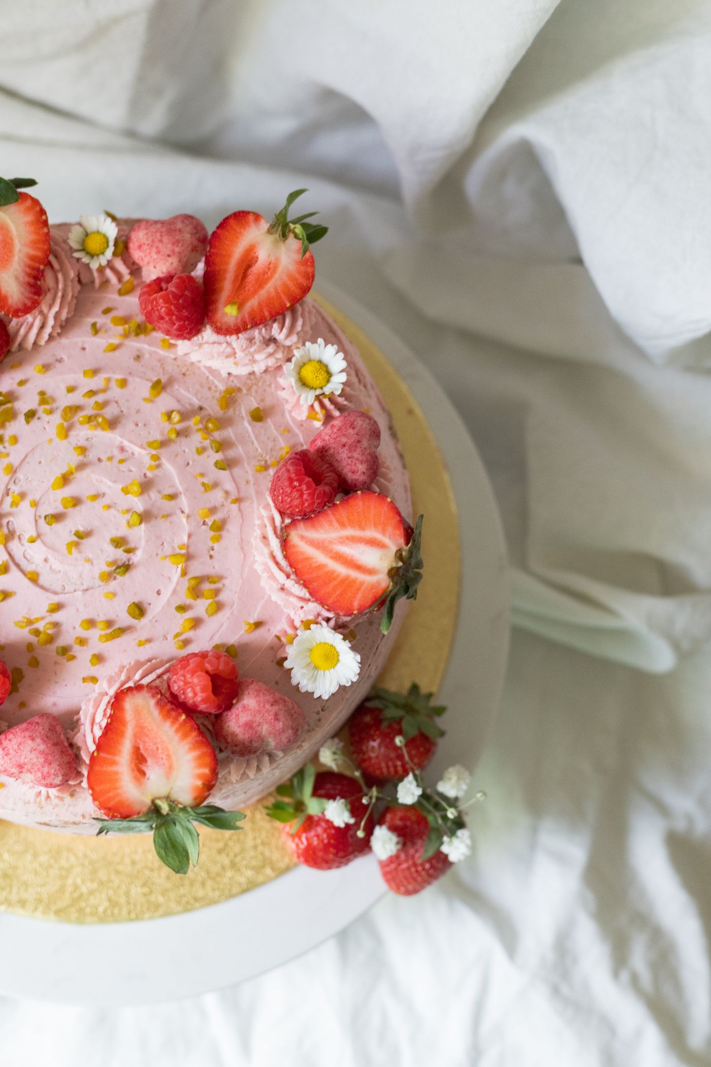 A fresh strawberry buttercream cake topped with strawberries, raspberries, and edible flowers